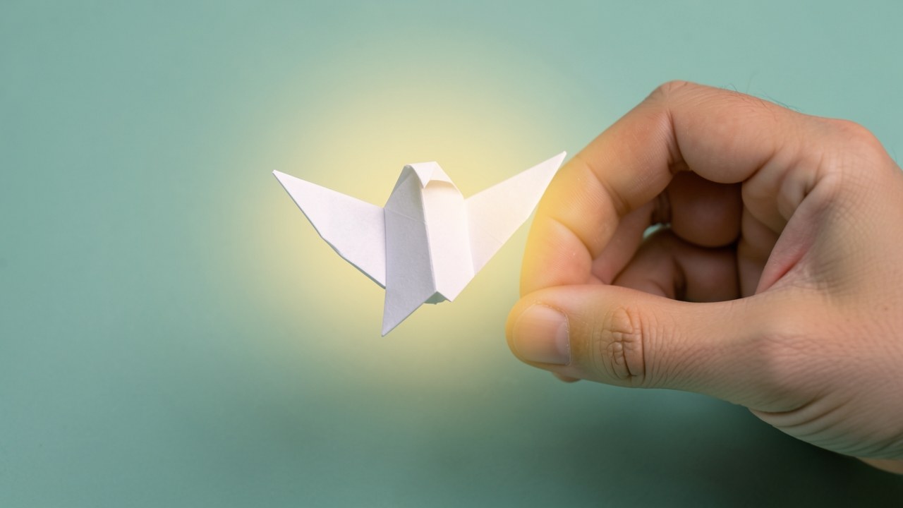 A hand releasing a small paper bird, symbolizing relief and forgiveness.